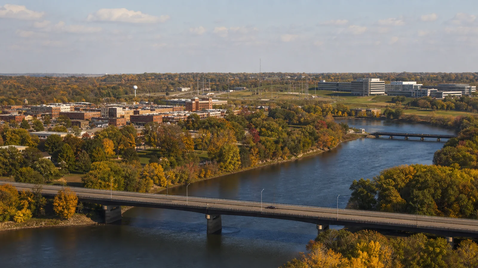 Editorial wide view of Minnesota River, historic brick downtown, river crossings, and modern manufacturing and corporate districts in Chaska