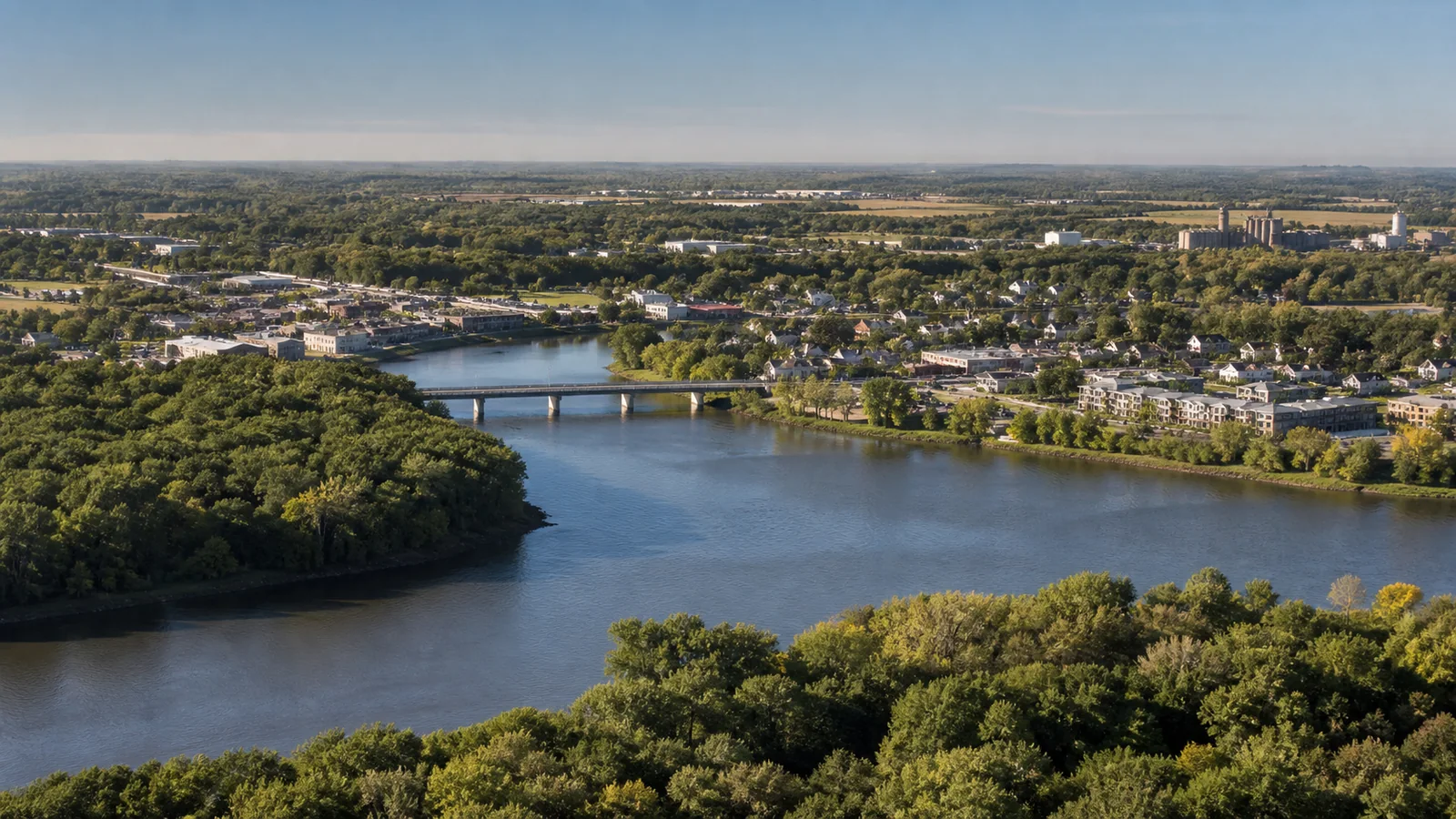 Editorial wide view of Mississippi and Elk River corridors, wooded banks, compact downtown, highway access, and employment districts in Elk River