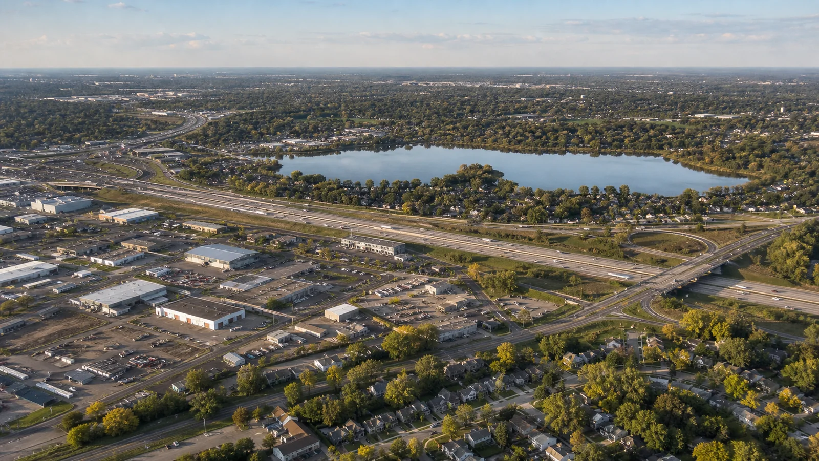 Editorial wide view of Lake Gervais and wooded parkland, mature neighborhoods, Rice Street, Interstate 35E and 694, commercial corridors, light industry, and redevelopment areas in Little Canada